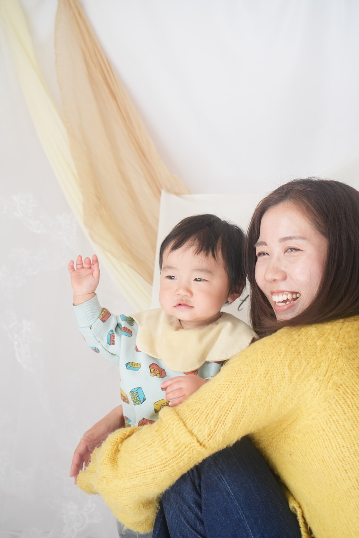 ママに抱っこされて手を振る赤ちゃん